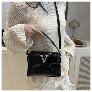 Detail of black crocodile texture handbag with silver V-shaped buckle and slim shoulder strap