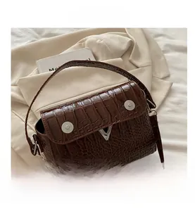 Detail of dark brown crocodile pattern leather handbag with silver V-shaped metal clasp