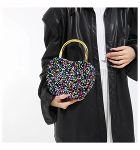 Detail of colorful sequin heart-shaped bag with gold metal handle worn by model