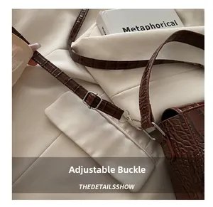 Detail of adjustable strap with silver buckle on brown crocodile texture handbag