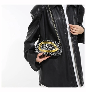 Close-up of glitter evening bag with oval metal buckle and chain strap on model