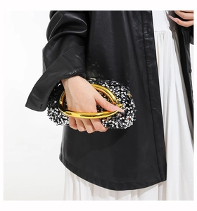 Close-up of black sequin evening clutch with a sculptural gold metal handle for women