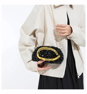 Detail view of sparkly black sequin evening clutch with golden C-shaped handle and chain