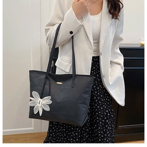 Détail du sac cabas en cuir noir avec charm fleur blanche et plaque dorée