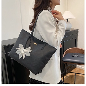 Detailansicht der schwarzen Leder-Shopper mit dekorativem Blumenanhänger und Metall-Logo