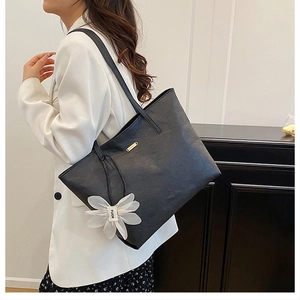 Detailansicht einer schwarzen geprägten Leder-Tote-Bag mit weißem Blumenanhänger und Metallschnalle