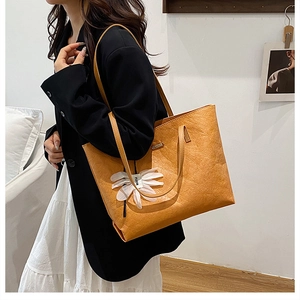 Macro detail of ginger yellow tote bag with pleated leather texture and daisy charm