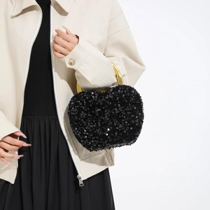Elegant black sequin handbag with gold circular metal handle shown in a fashion lifestyle view