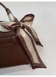 Vue détaillée d'un sac à main en cuir marron avec un foulard en soie noué sur la poignée