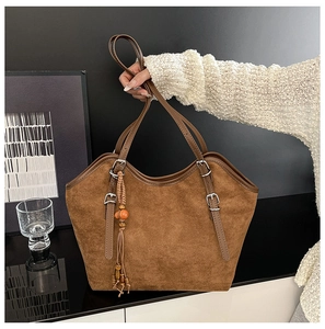 Detail of brown faux suede tote bag featuring a leather strap and beaded tassel charm