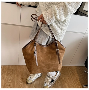 Detail of a large brown suede tote bag with dark leather straps and silver metal buckles