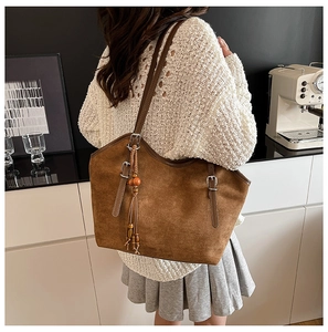 Detail of a brown suede tote bag featuring adjustable strap and bohemian tassel ornament