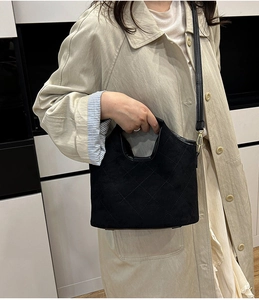 Chic black quilted bucket bag with gold hooks worn by a model in a beige coat