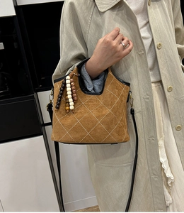 Detail of brown suede bucket bag featuring white quilted diamond patterns and beaded charm