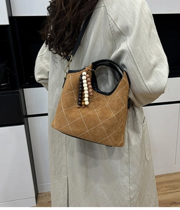 Brown quilted bucket bag with wooden bead charm worn with a long trench coat