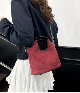 Model wearing a wine red quilted bucket bag with black leather straps in a minimalist setting