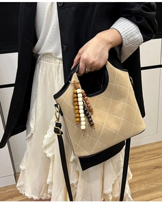 Detail of khaki quilted bucket bag with beaded tassel charm and black leather handle
