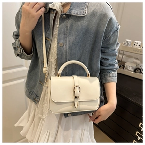 Close-up of cream white handbag with gold buckle on a model in a cozy indoor setting