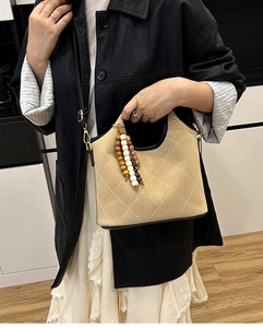 Close-up of quilted beige bucket bag with wooden bead charm detail and black edge finish