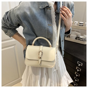 Model wearing a cream square leather handbag with gold buckle and adjustable strap