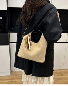 Detail of beige quilted bucket bag with wooden bead tassel and black top handles