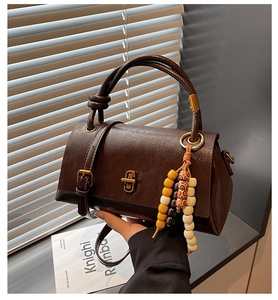 Detail of dark brown vintage handbag with embossed leather texture and wooden bead pendant