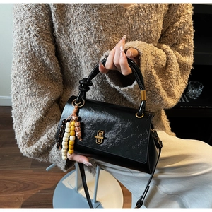 Detail of black pleated faux leather handbag with gold clasp and colorful bead charm