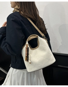 Detail of white quilted bucket bag with brown trim and colorful beaded tassel charm