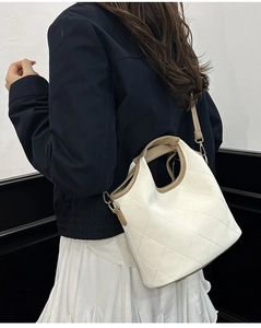 Detailed look at the quilted texture and contrast strap of the white bucket bag on a model