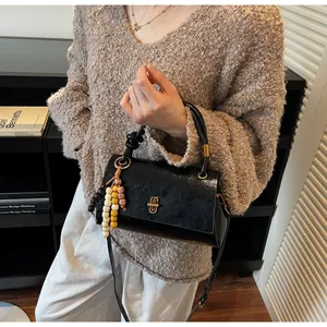 Detail of black glossy PU leather handbag with gold buckle and colorful beaded charm