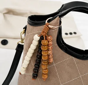 Detail of brown suede bucket bag with white diamond stitching and beaded tassel charm