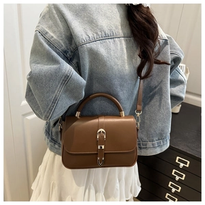 Brown leather crossbody bag with top handle and gold buckle worn by model in studio