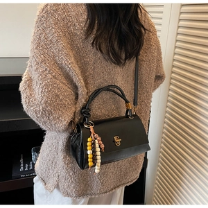 Detail of black pebbled leather handbag featuring gold clasp and colorful bead charm