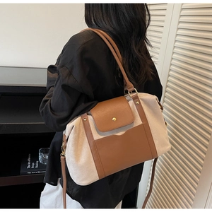 Détail du sac à bandoulière bicolore en toile avec finitions en cuir brun et fermoir métal