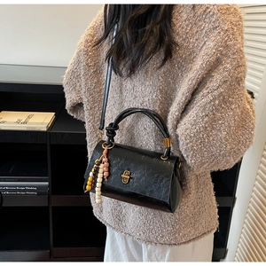 Detail of black patent leather crossbody bag with gold twist lock and colorful beaded charm
