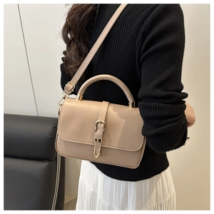 Detail of elegant beige crossbody bag with gold metallic buckle closure worn by a model