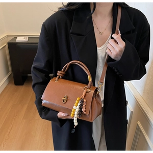 Detail of vintage brown leather handbag with a golden twist lock and colorful bead charm