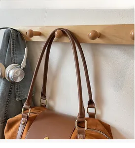 Détail du sac fourre-tout en daim marron avec boucles en métal doré sur un crochet en bois