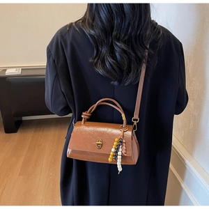 Detail of a brown leather handbag with a unique beaded charm and metallic rotary lock
