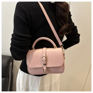 Pale pink leather satchel handbag with gold buckle shown on a model in a minimalist setting