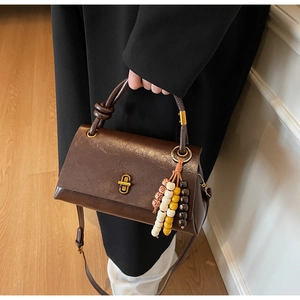 Detail of vintage brown leather handbag featuring colorful ethnic bead pendant and gold lock