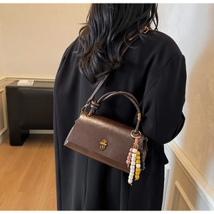 Deep brown retro handbag with metallic twist lock and beaded tassel shown on a shoulder