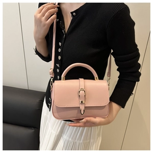 Detail of pink fashion handbag with gold buckle and top handle worn by a model