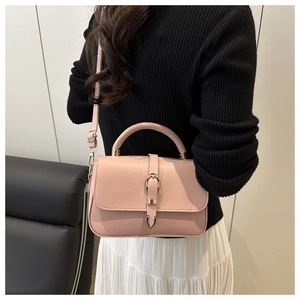 Detail of pink crossbody bag featuring gold horseshoe buckle and smooth leather texture