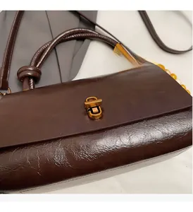 Close-up of glossy brown oil wax leather handbag with retro gold metal twist lock and beads