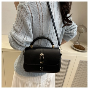 Detail of black lychee grain crossbody bag with gold buckle on a cream interior background