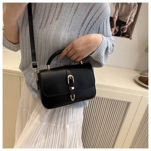 Detail of minimalist black crossbody bag with gold hardware shown on a model