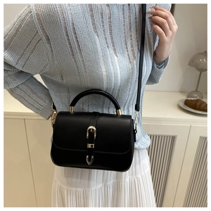 Detail of elegant black faux leather handbag featuring a golden buckle and slim strap