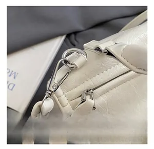 Close-up of silver metal hook and strap detail on white textured leather handbag