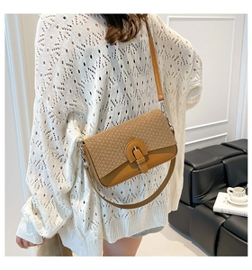 Detail of a brown leather crossbody bag with woven flap and metal buckle on a model